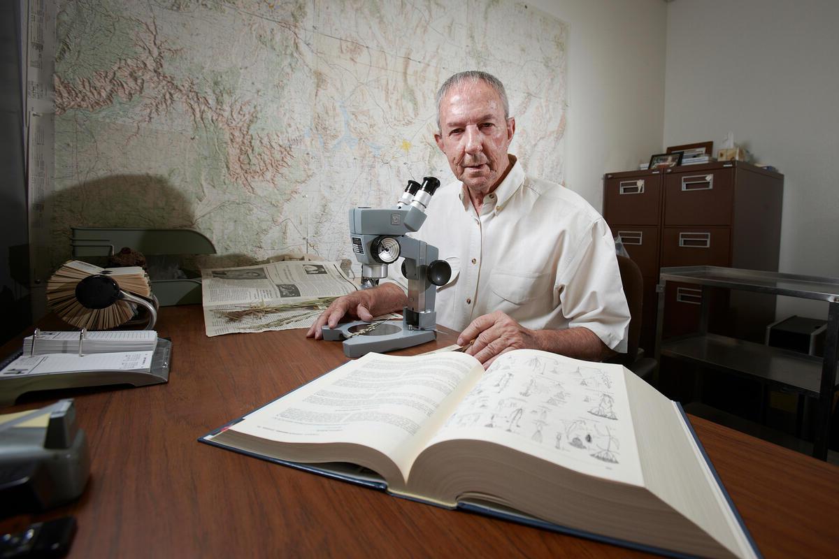 一个男人坐在桌子旁，拿着显微镜和打开的书