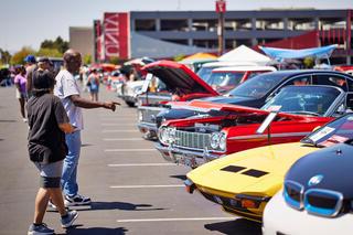 man pointing out a car to a female companion during car show in parking lot